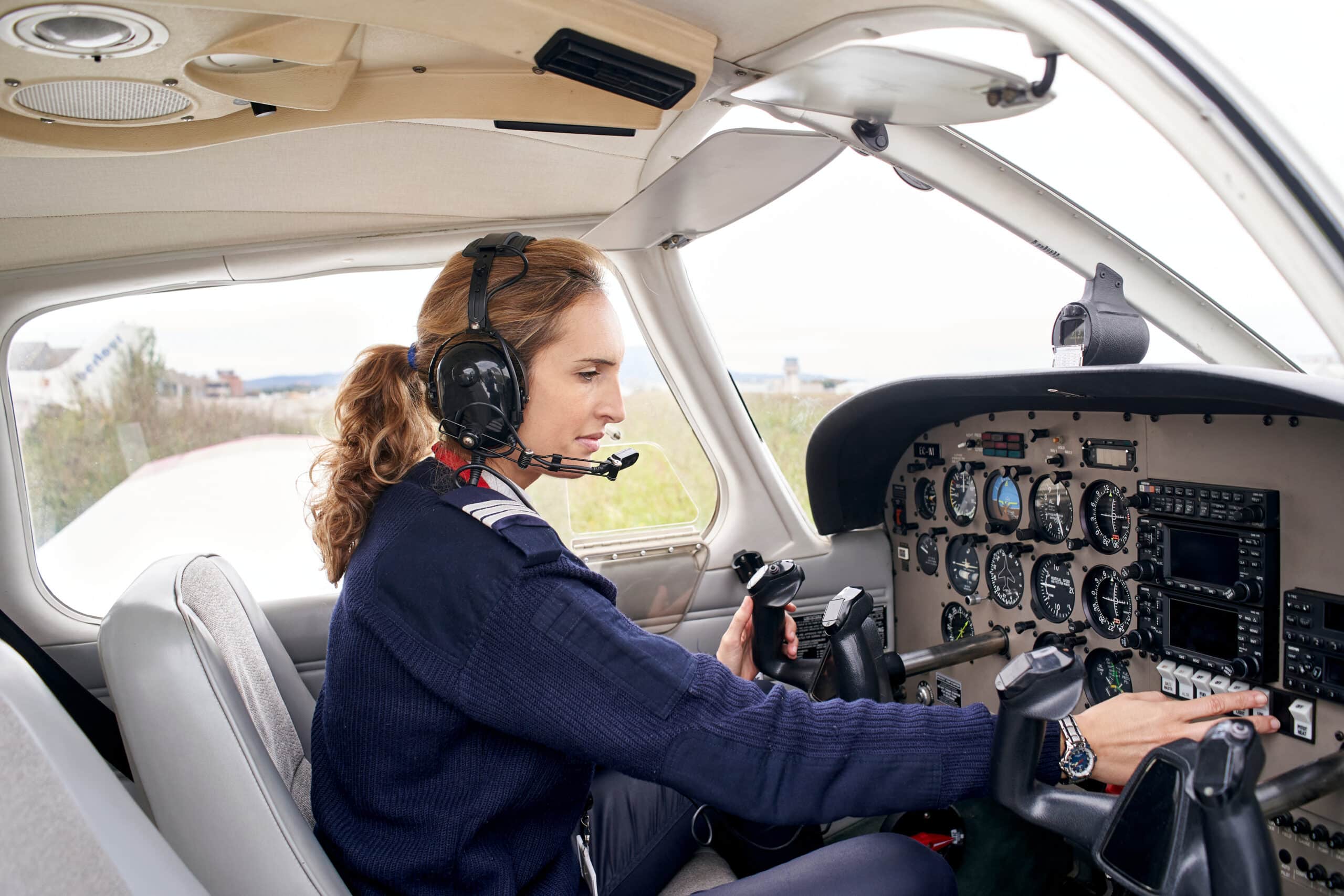 Side view of a female pilot in the cockpit of an airplane touching some buttons.