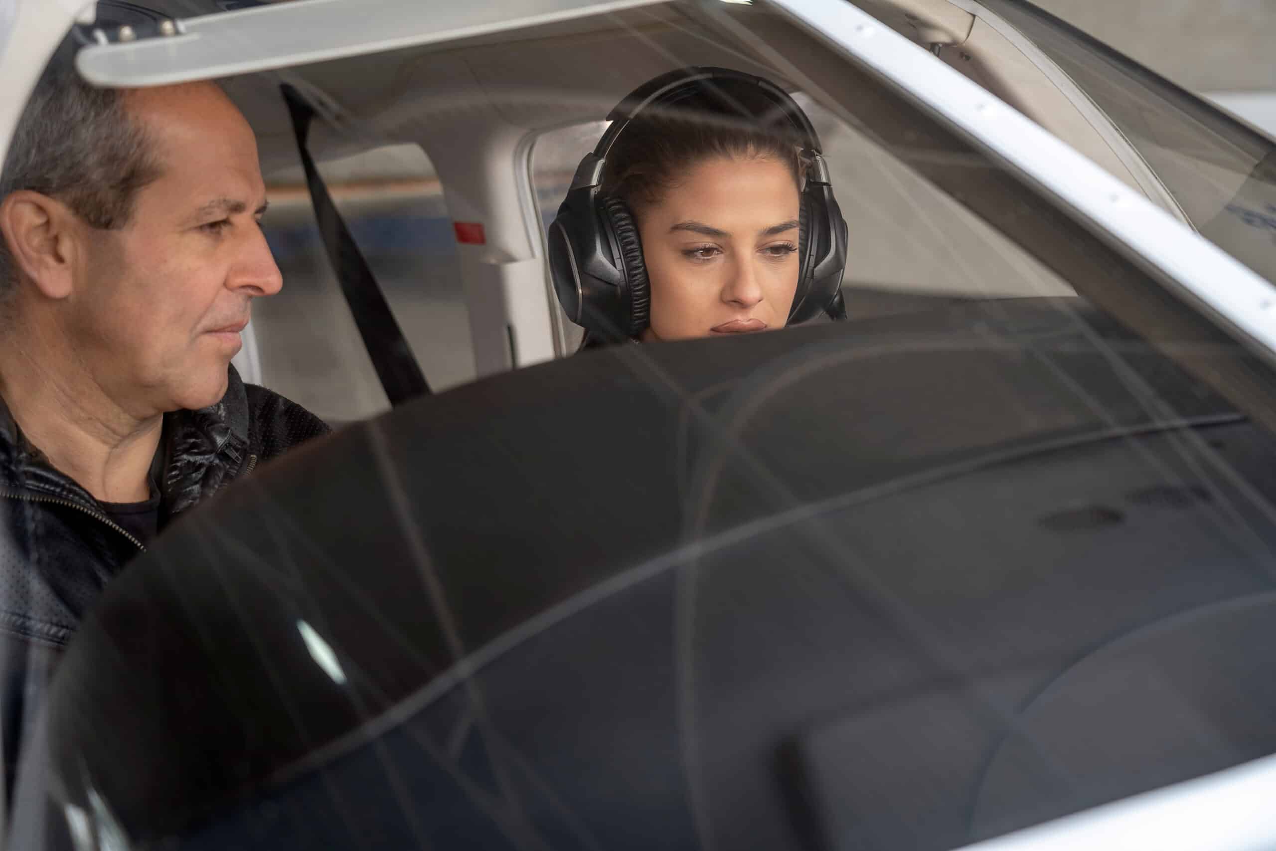 Portrait of attractive young woman trainee pilot with headset preparing to fly. She is sitting next to istructor and looking at dashboard of the private plane.